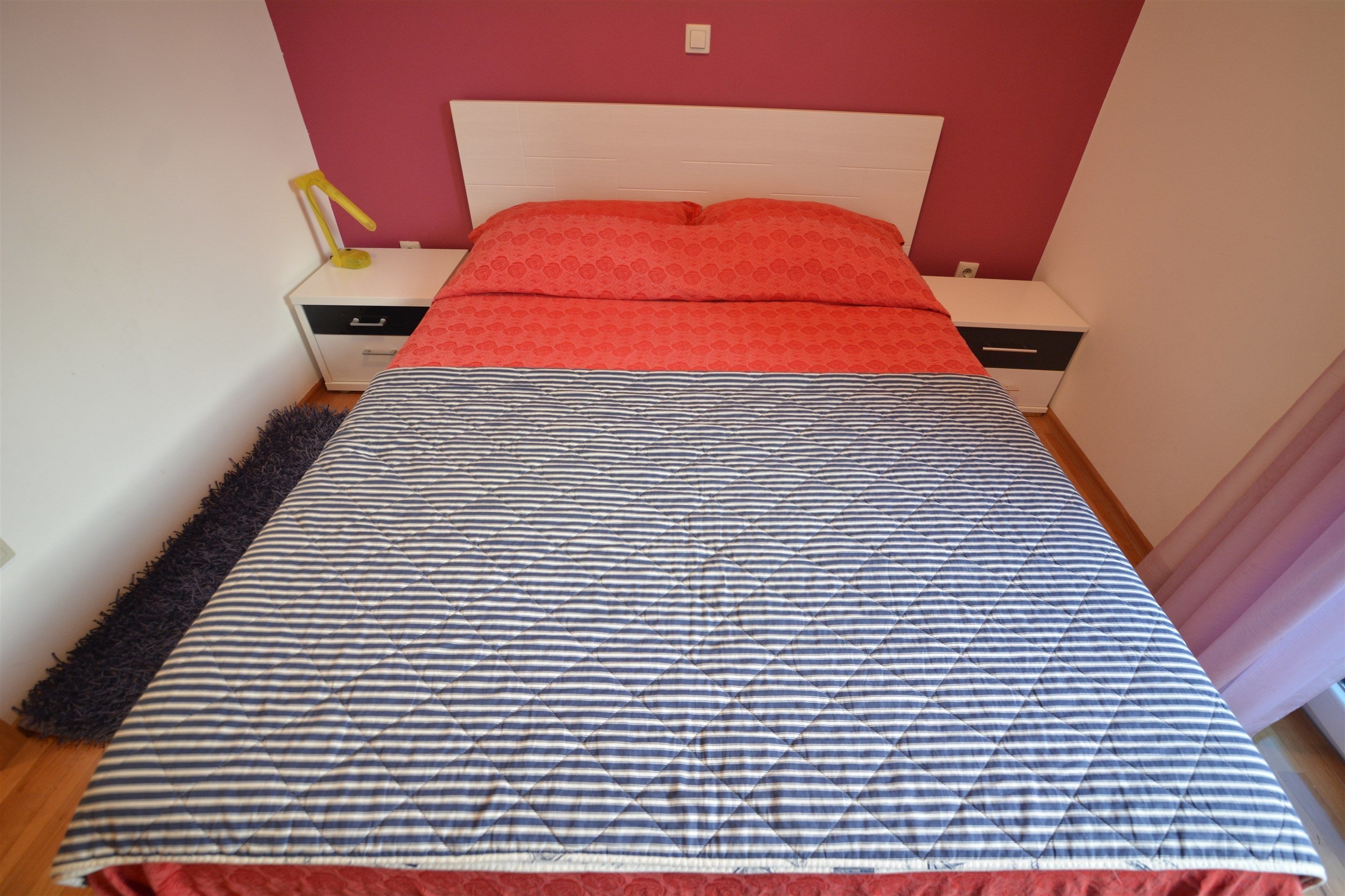 Un dormitorio con cama, dos mesitas de noche, una lámpara y una manta blanca y roja a rayas.