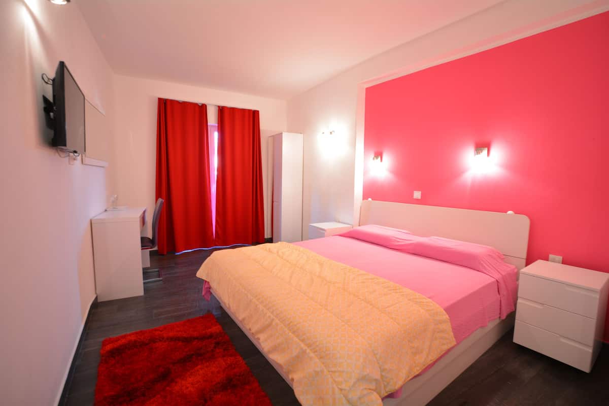 A bedroom with a bed, nightstands, a TV, and a red curtain.