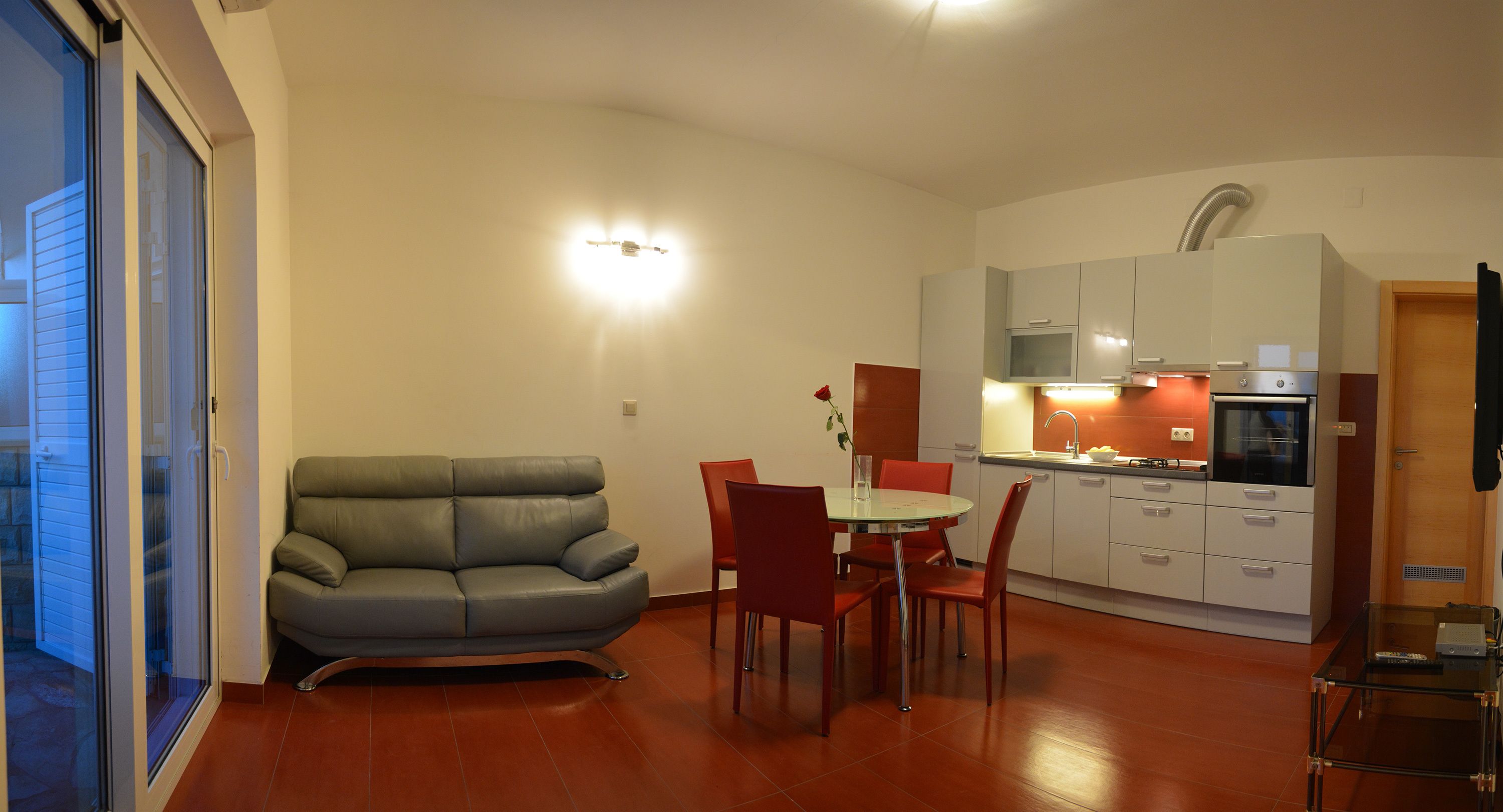 A compact living space with a sofa, dining table, chairs, a kitchenette, and a sliding glass door.