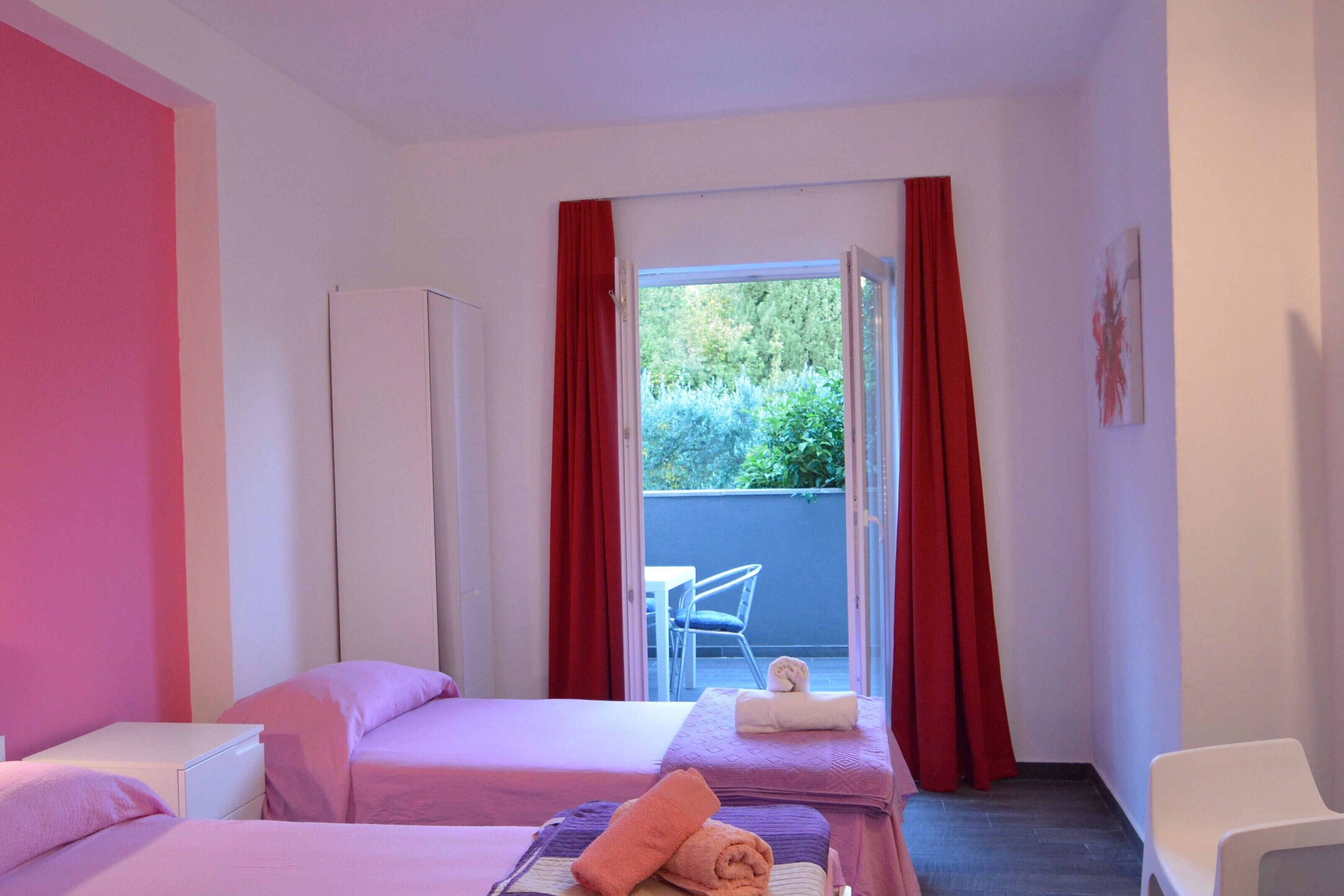 A hotel room with two beds, a wardrobe, and a view of the outside.