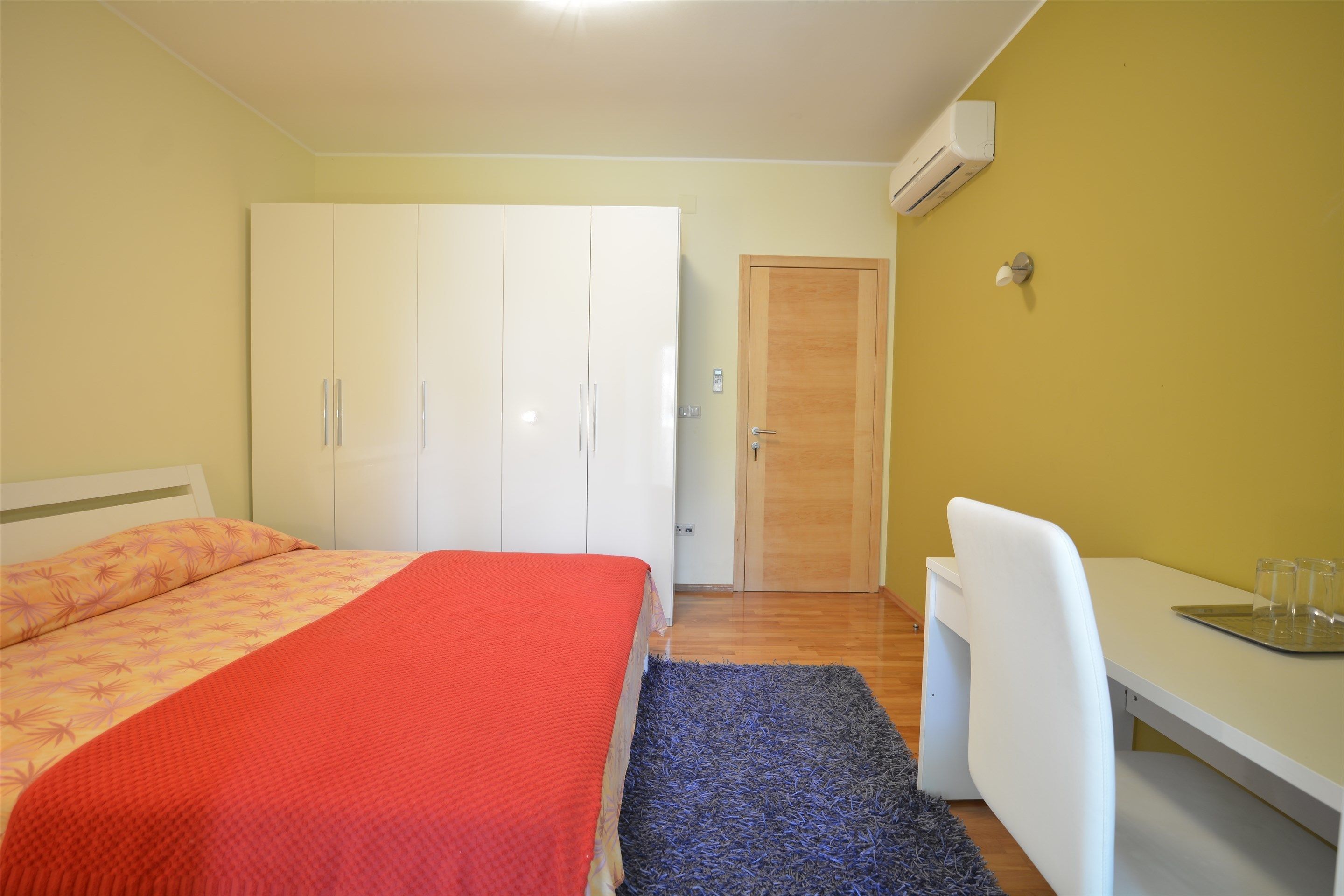 A bedroom with a bed, a desk, and a wardrobe.