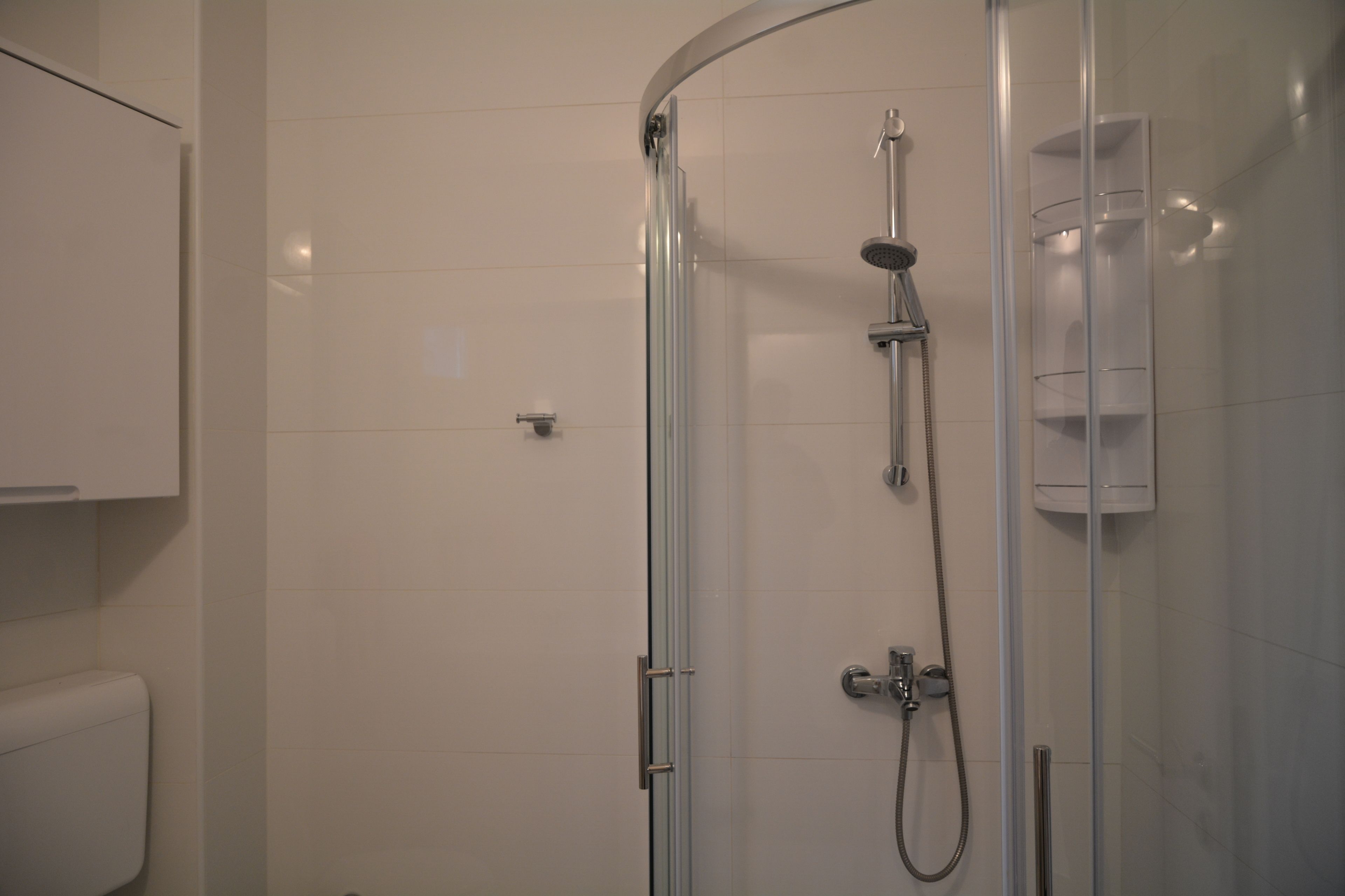 A glass-enclosed shower with a handheld showerhead and a wall-mounted faucet.