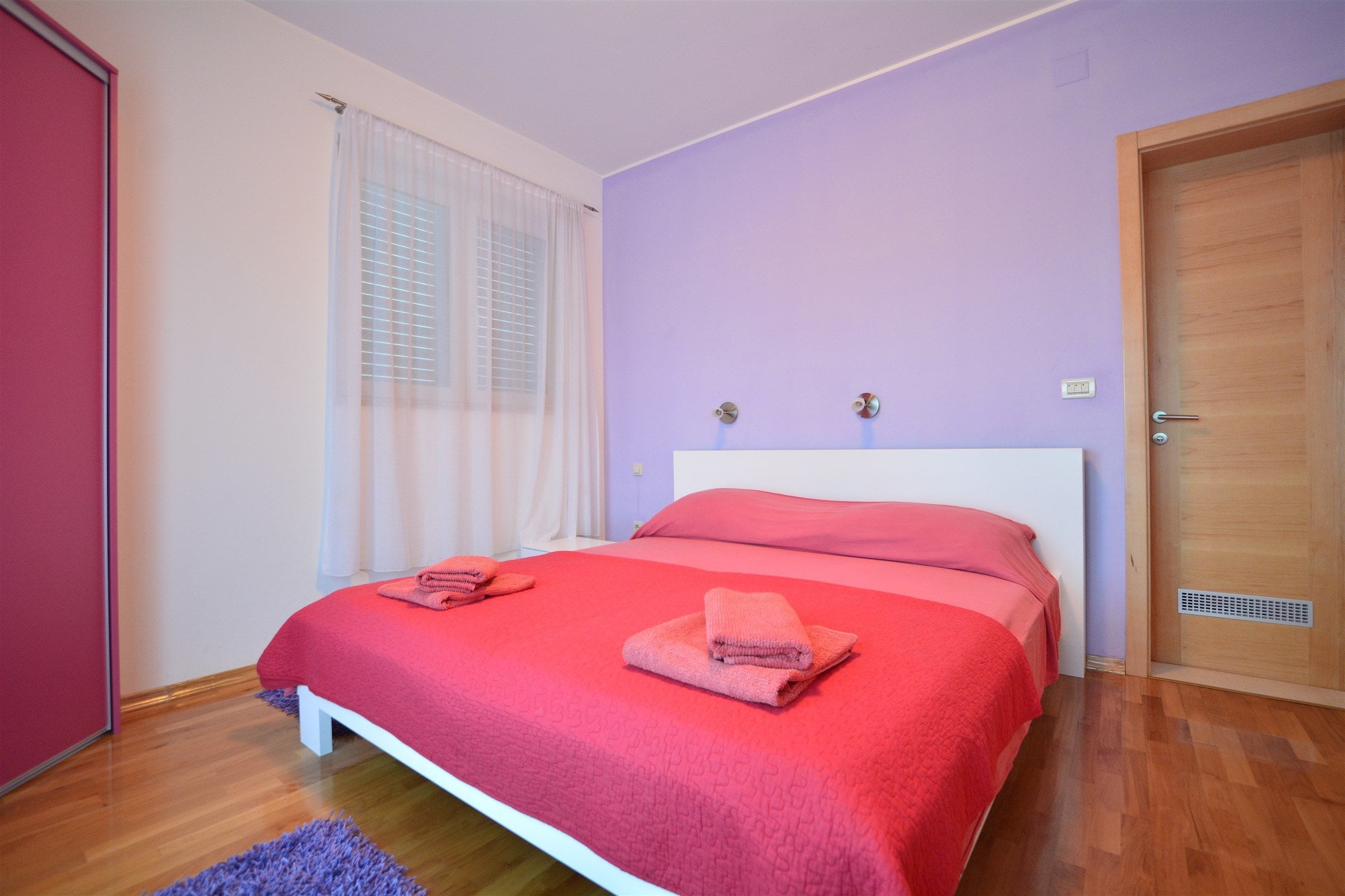 A bedroom with a bed, a door, and a window with curtains.
