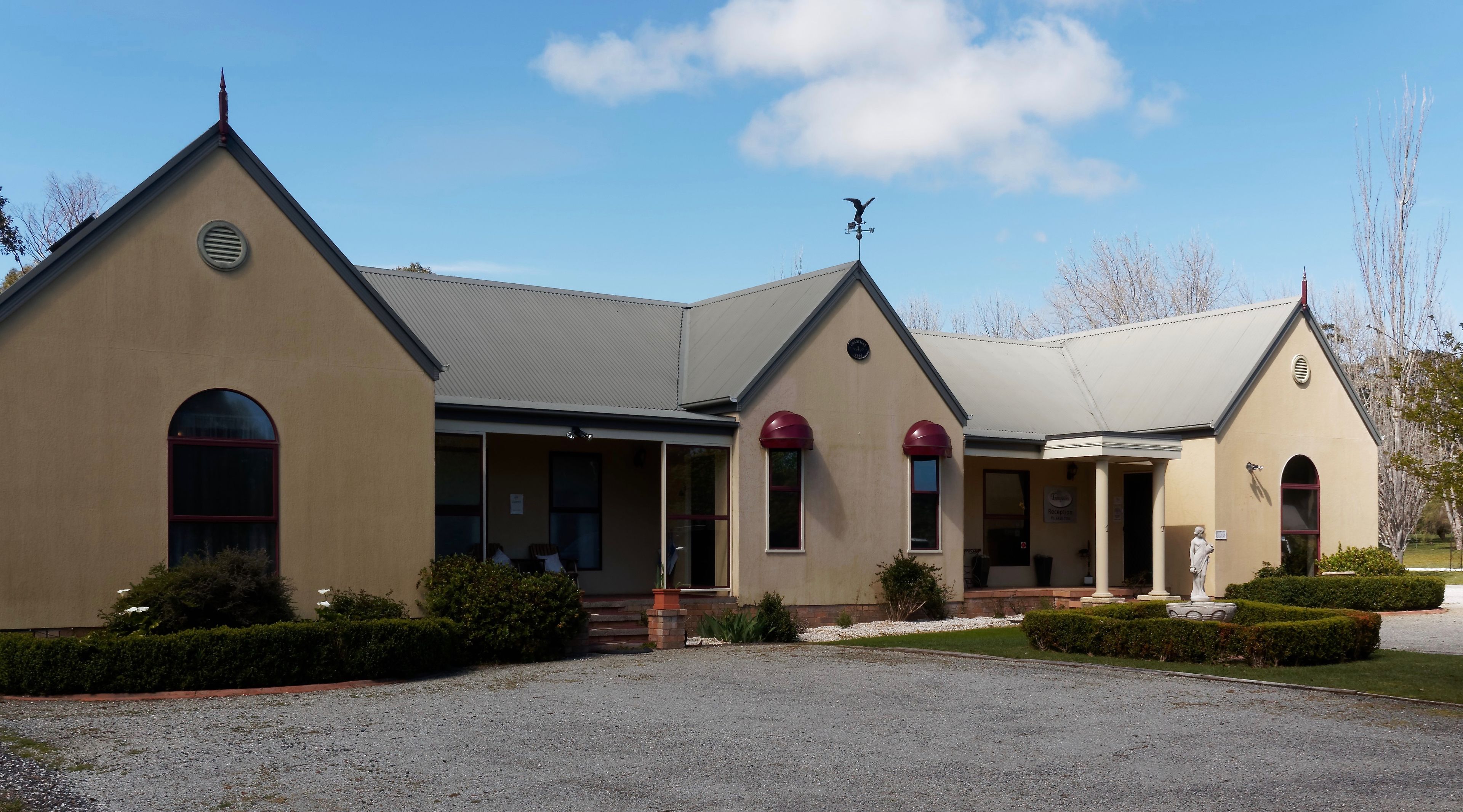 A building with a gabled roof, a weather vane, and a statue in front.