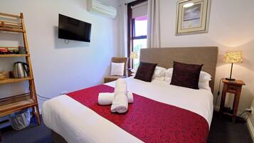 Habitación de hotel con cama, televisor, ventana con cortinas, estante de madera y lámpara.