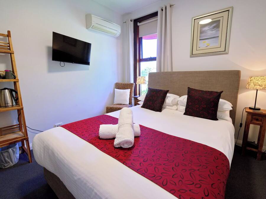 Habitación de hotel con cama, televisor, ventana con cortinas, estante de madera y lámpara.