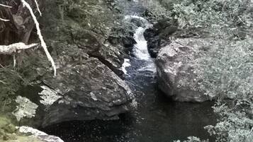 Un arroyo serpentea a través de un terreno rocoso con grandes rocas y vegetación densa.