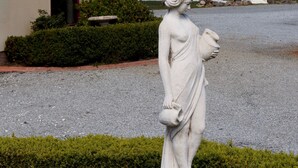 Una estatua de una mujer sosteniendo una jarra frente a un edificio con una puerta y una ventana.