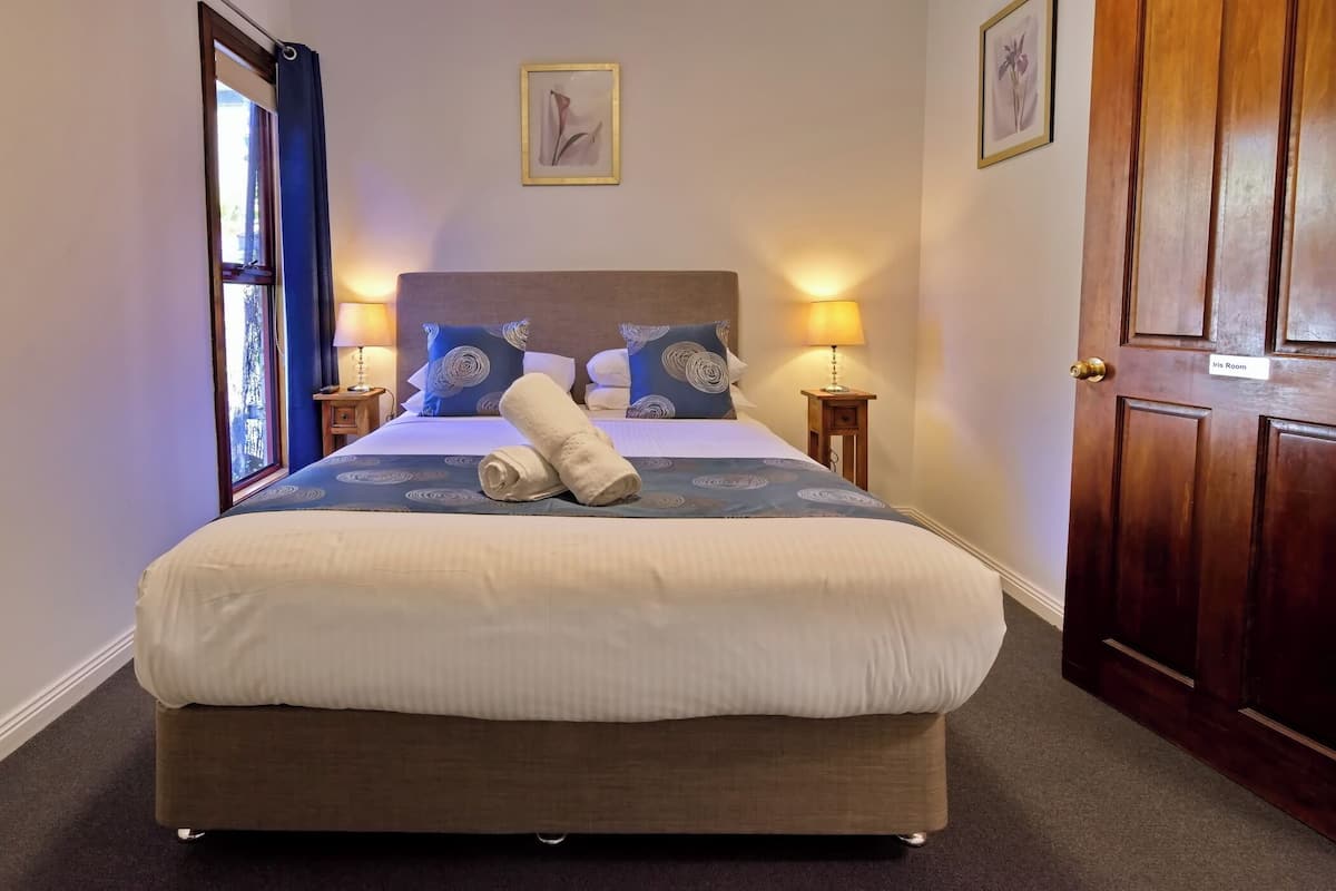 A neatly made bed with a rolled towel, two bedside lamps, a framed picture on the wall, and a door labeled "Iris Room".