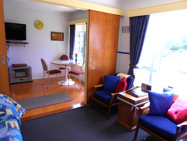 Una habitación con una mesa de comedor, sillas, un televisor y una puerta de madera que da a un área exterior.