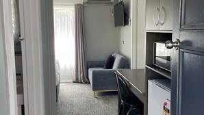 Un ambiente compatto con angolo cottura, un divano grigio, un piccolo tavolo da pranzo e una ventola a soffitto.