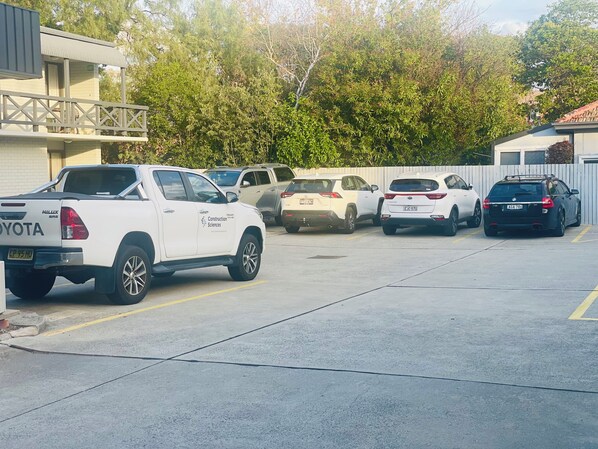A parking lot with several vehicles, including a white Toyota truck and a white SUV. - Parkway Motel (Queanbeyan)