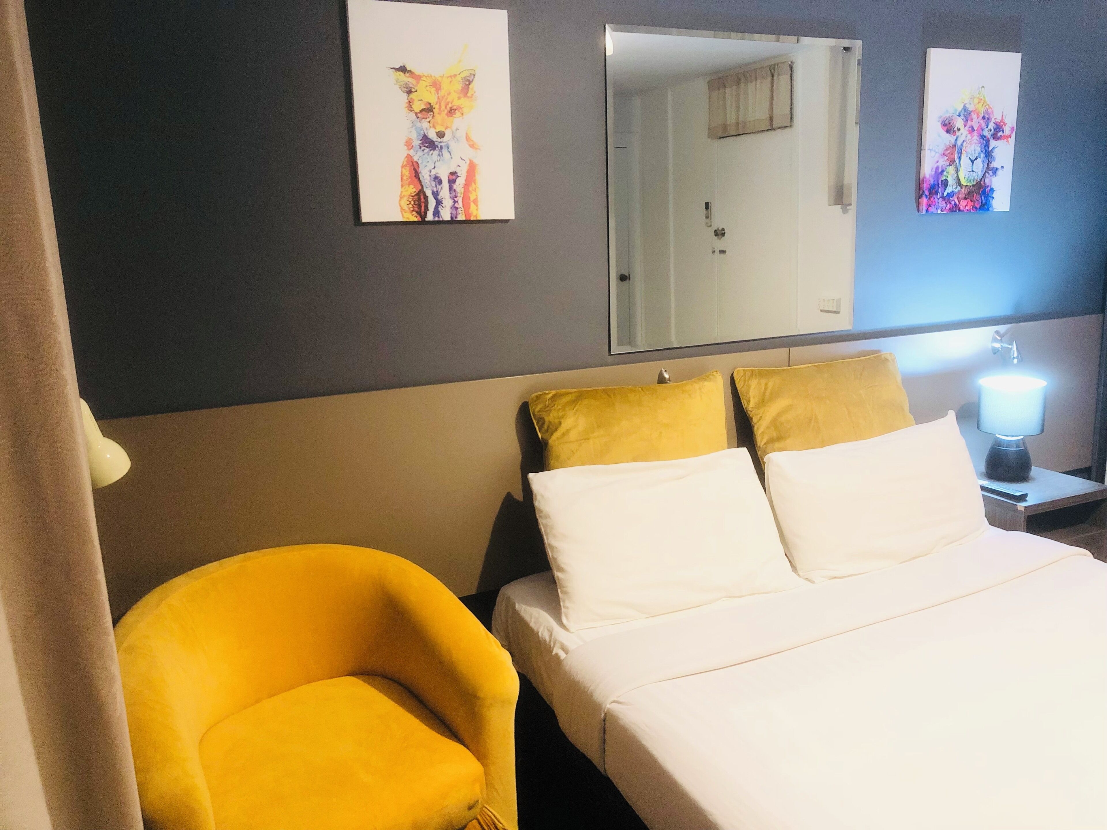 Ein Hotelzimmer mit Bett, zwei Kissen, einem Nachttisch mit Lampe und zwei an der Wand hängenden Bildern.