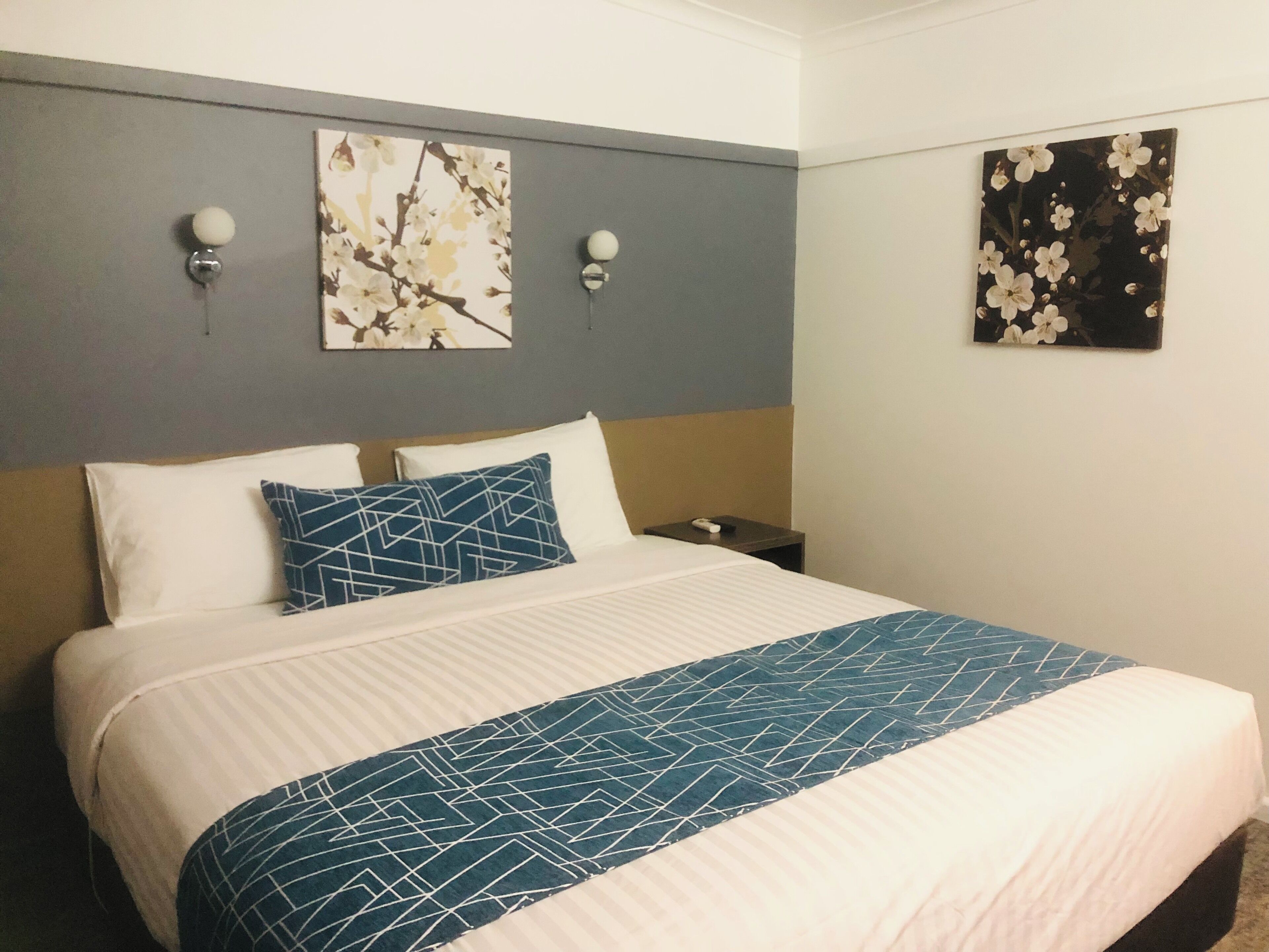 A hotel room with a bed, two wall-mounted lamps, and two framed floral artworks.
