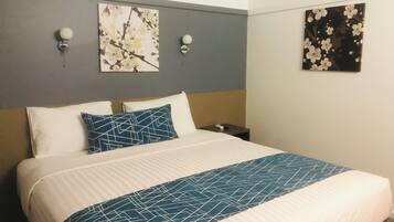 A hotel room with a bed, two wall-mounted lamps, and two framed floral artworks.