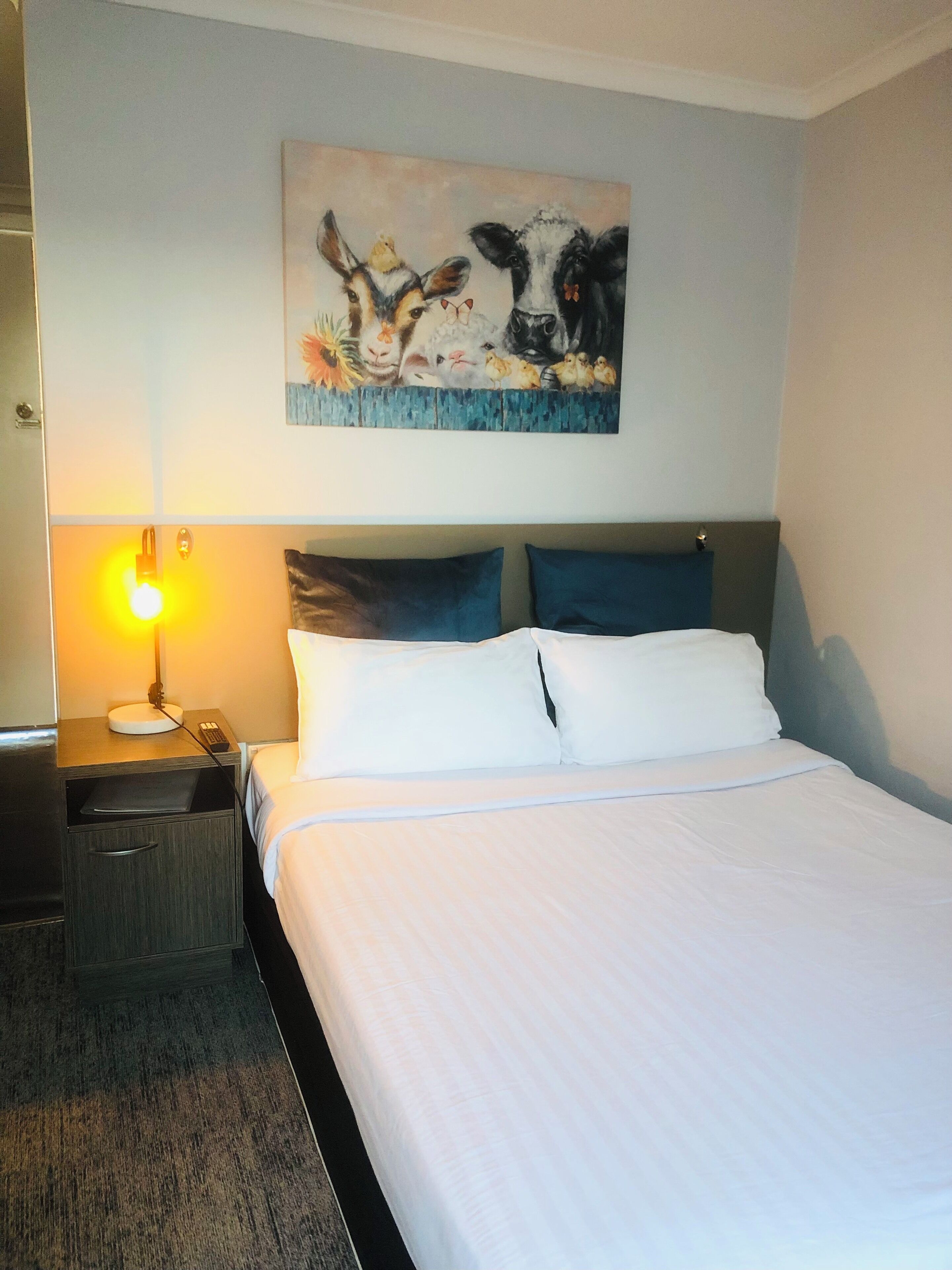 Ein Hotelzimmer mit Bett, Nachttisch, Lampe und einem Wandbild mit Tieren.