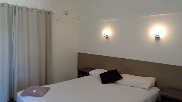 Una camera d'albergo con un letto, due luci a parete, una tenda e un comodino.