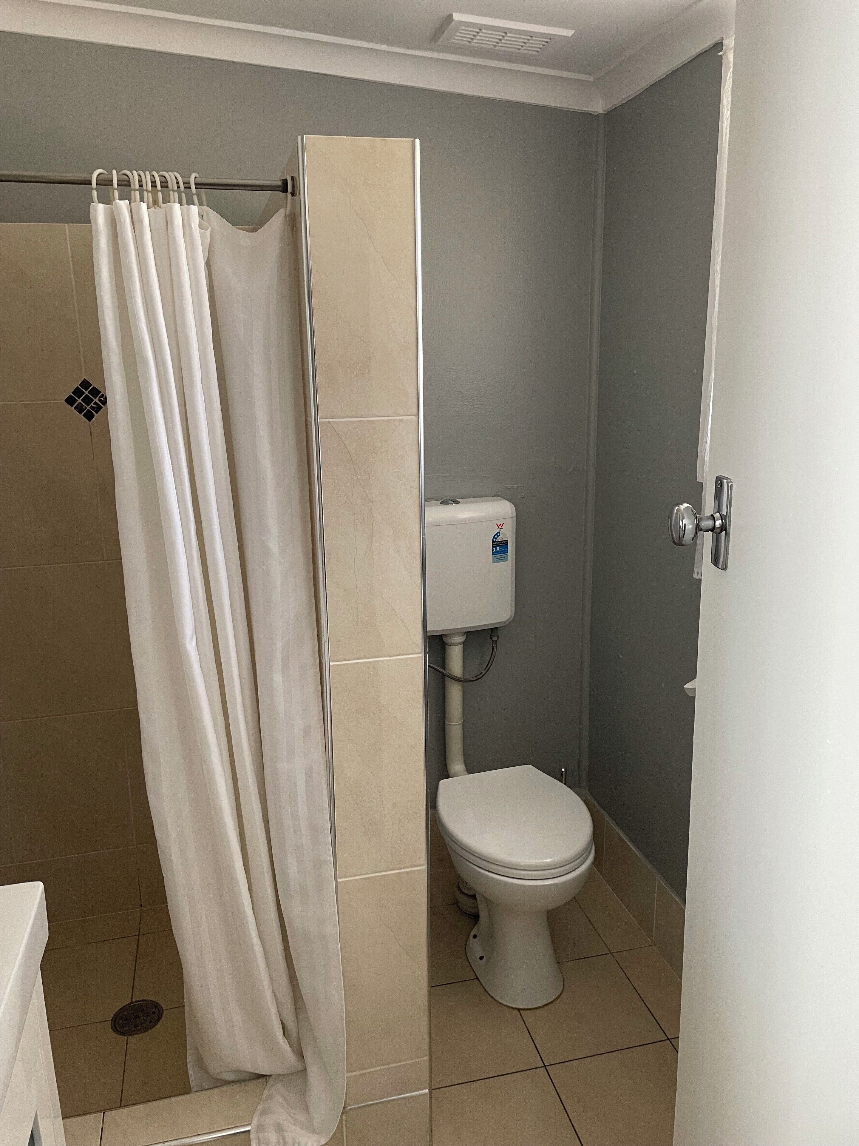 Een badkamer met douchegordijn, toilet en betegelde muren.