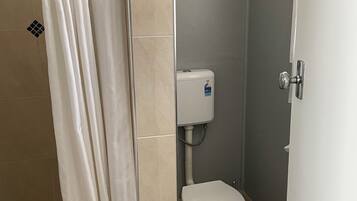 Een badkamer met douchegordijn, toilet en betegelde muren.