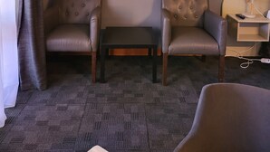 Camera d'albergo con due poltrone in pelle, un tavolino, un'opera d'arte incorniciata a parete e un comodino con lampada e telecomando.