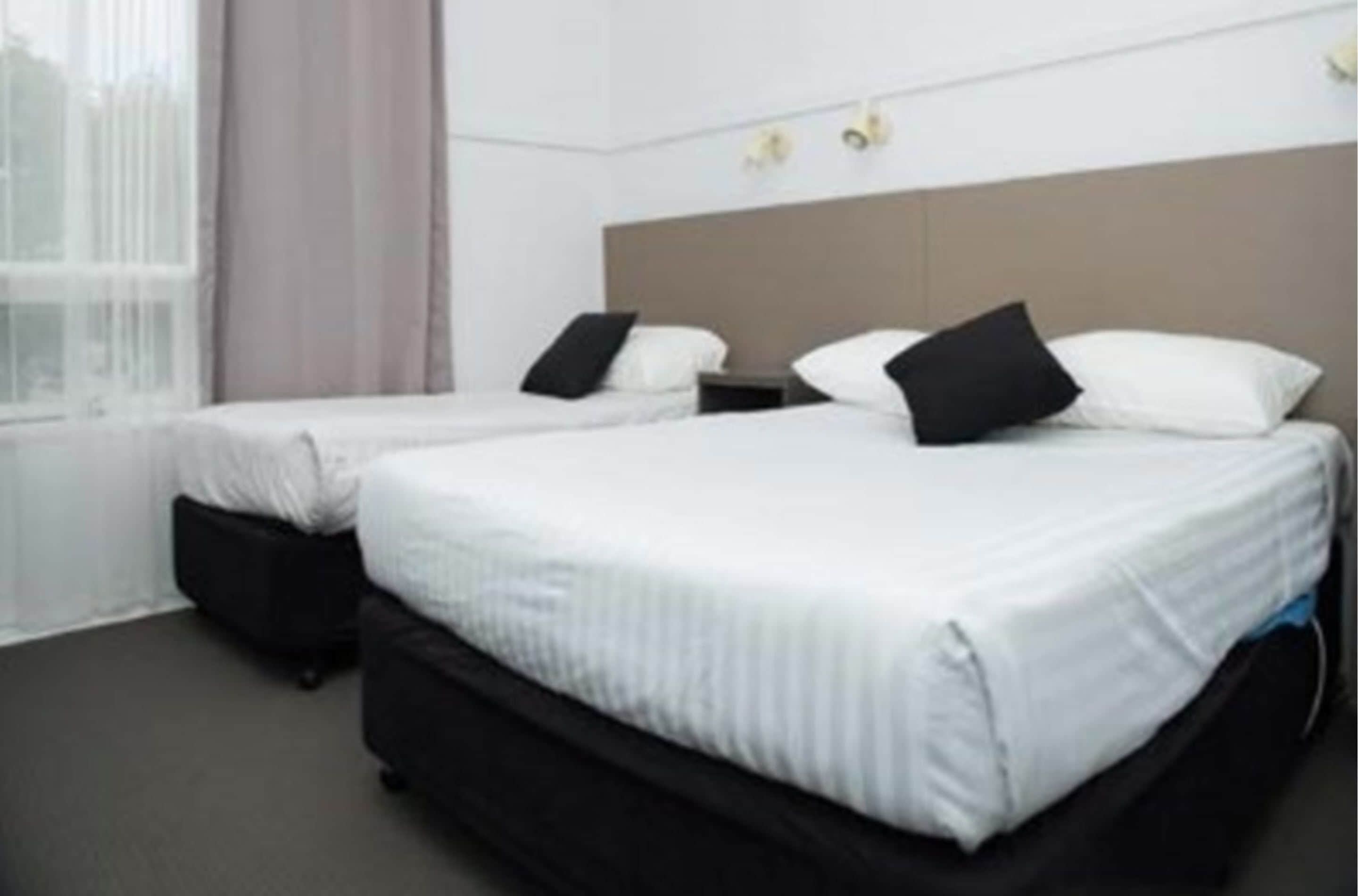 Een hotelkamer met twee eenpersoonsbedden, een nachtkastje en een raam met gordijnen.