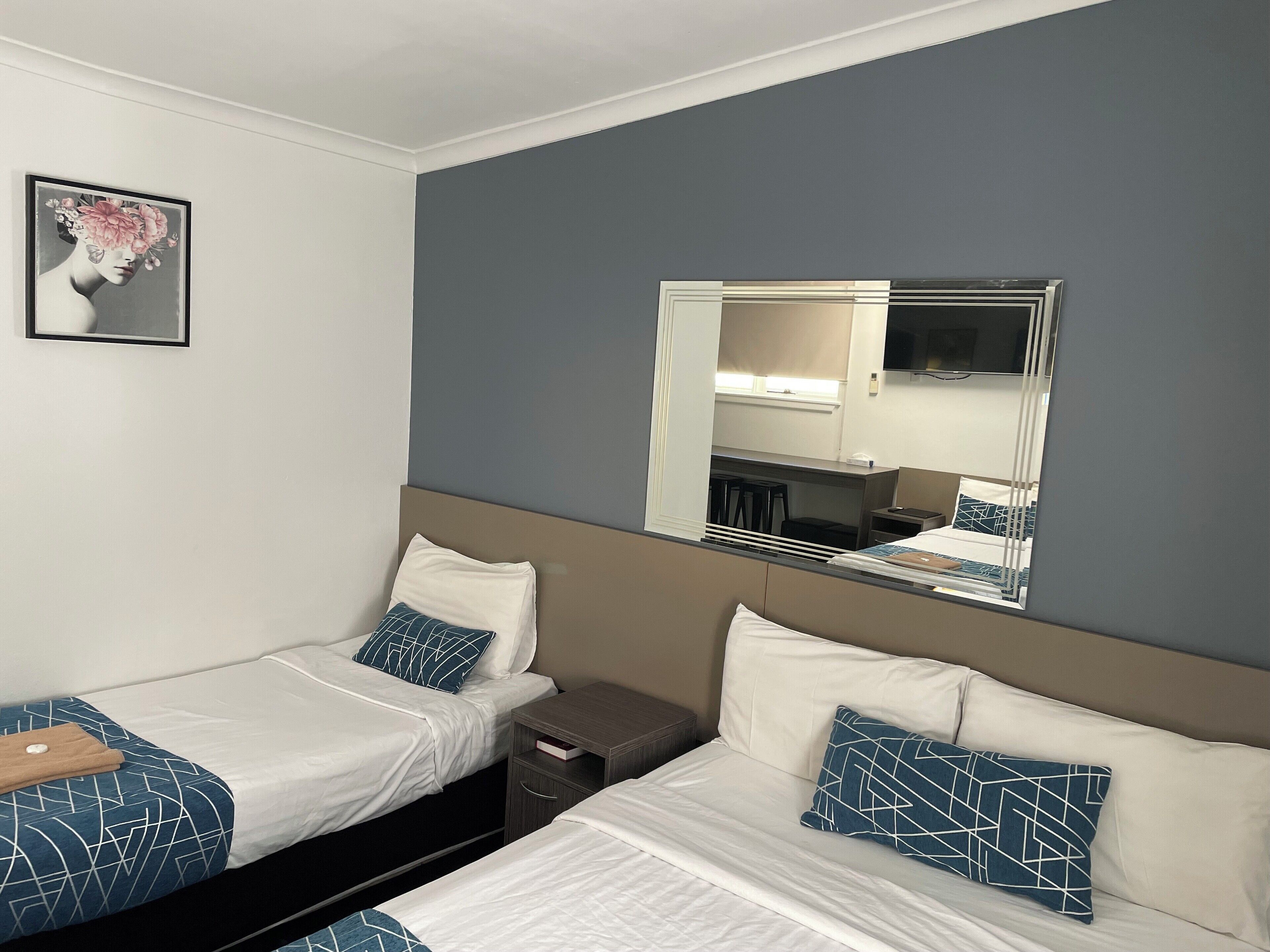 A hotel room with two beds, a large mirror, a small desk, and a nightstand.
