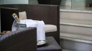 A wicker chair with a white cushion, a small table with a white napkin, a glass, and a bottle of champagne. - Hotel Aquadolce (Verbania)