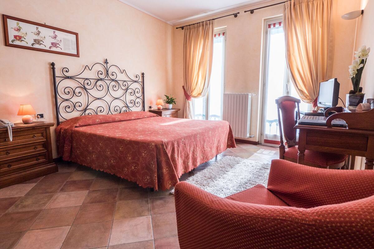 A bedroom with a bed, a desk, a chair, a dresser, and a window with curtains.