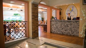A hotel reception area with a stone counter, a receptionist, and a view of the dining area. - Hotel Aquadolce (Verbania)