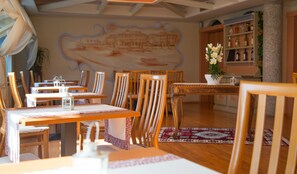 Un restaurante con mesas y sillas de madera, un mural en la pared y una estantería con botellas.
