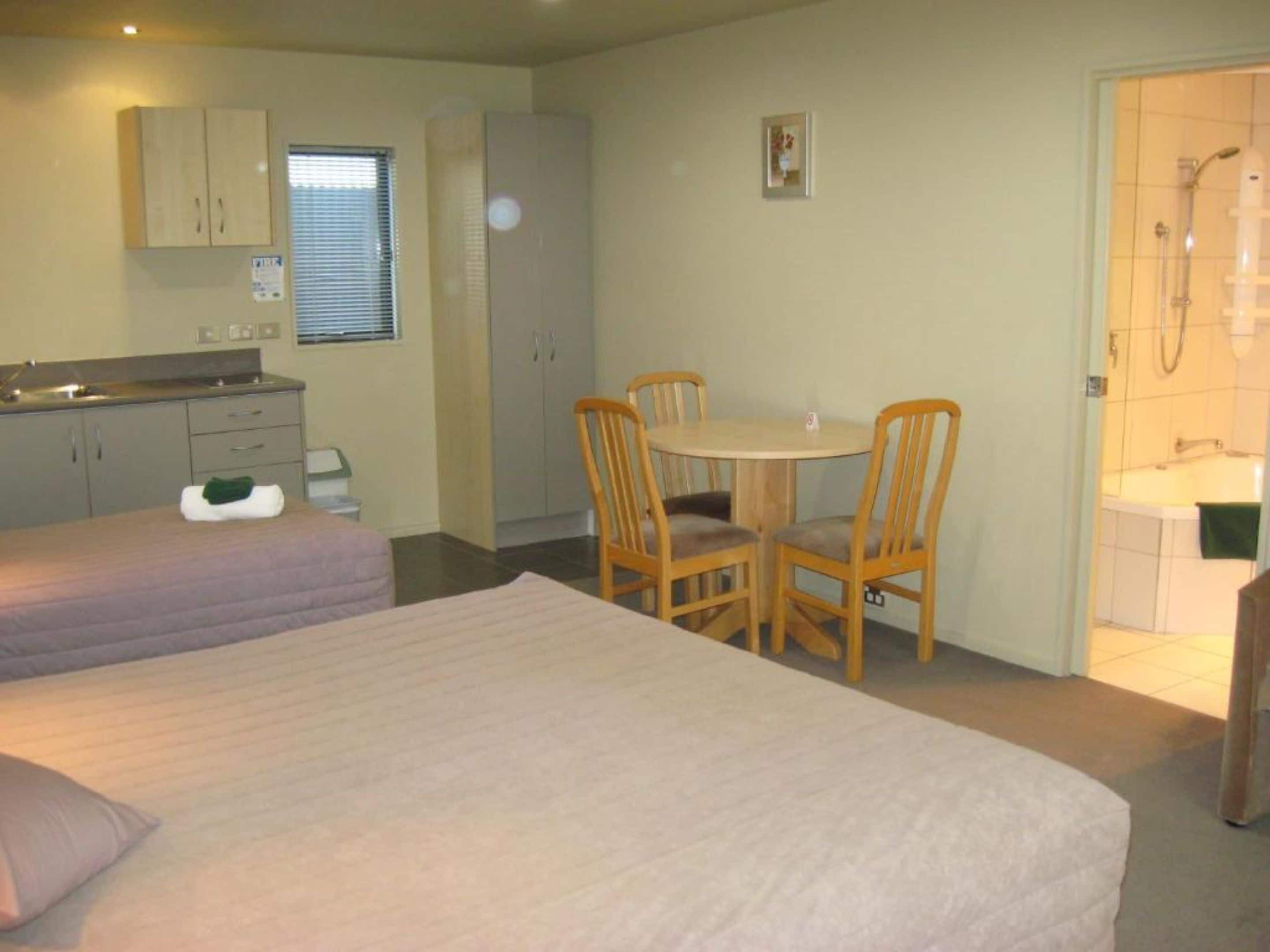 Une chambre d’hôtel avec deux lits, une petite kitchenette, une table à manger avec des chaises et une salle de bain avec douche.
