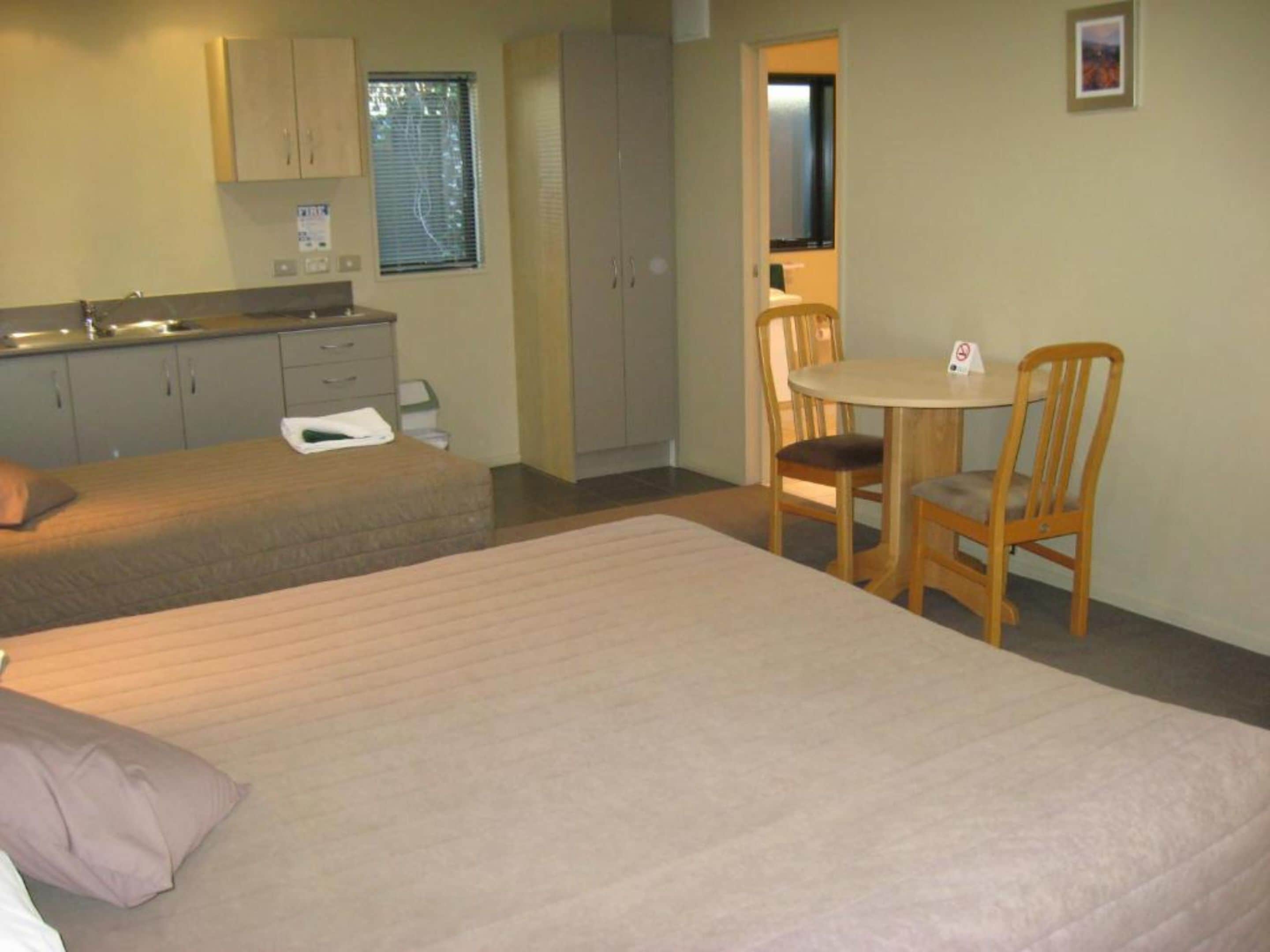 A room with a bed, a small table with two chairs, a kitchenette, and a door leading to another room.