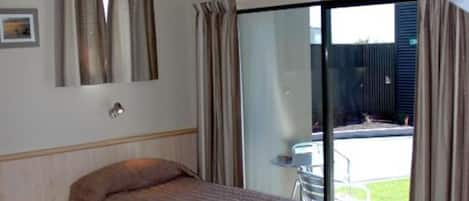 A hotel room with two beds, a large window with curtains, a ceiling fan, and a view of the outside.