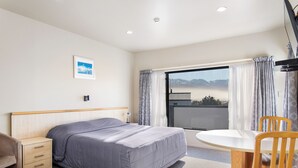 A hotel room with a bed, bedside table, chair, and a view of mountains through the window. - Kaikoura Gateway Motor Lodge (Kaikoura)
