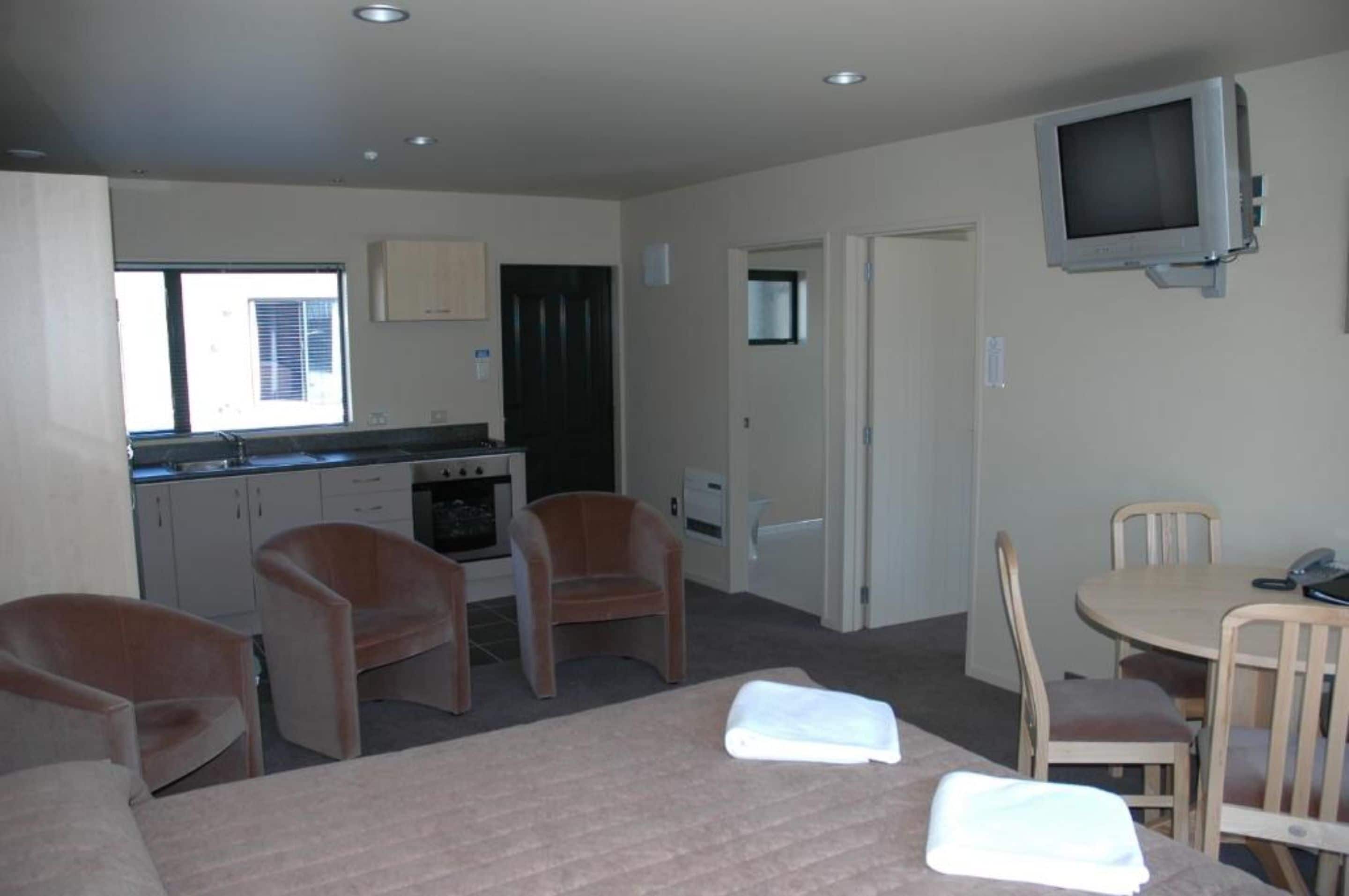 A compact room with a kitchenette, a dining area, and a TV mounted on the wall.