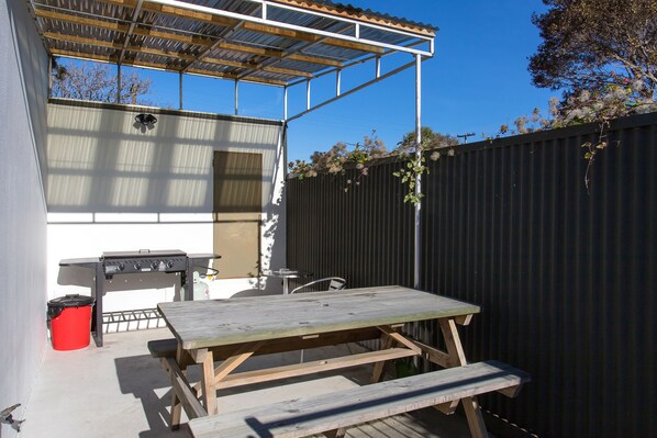A patio with a wooden table and benches, a barbecue grill, and a covered area with a metal roof. - Kaikoura Gateway Motor Lodge (Kaikoura)