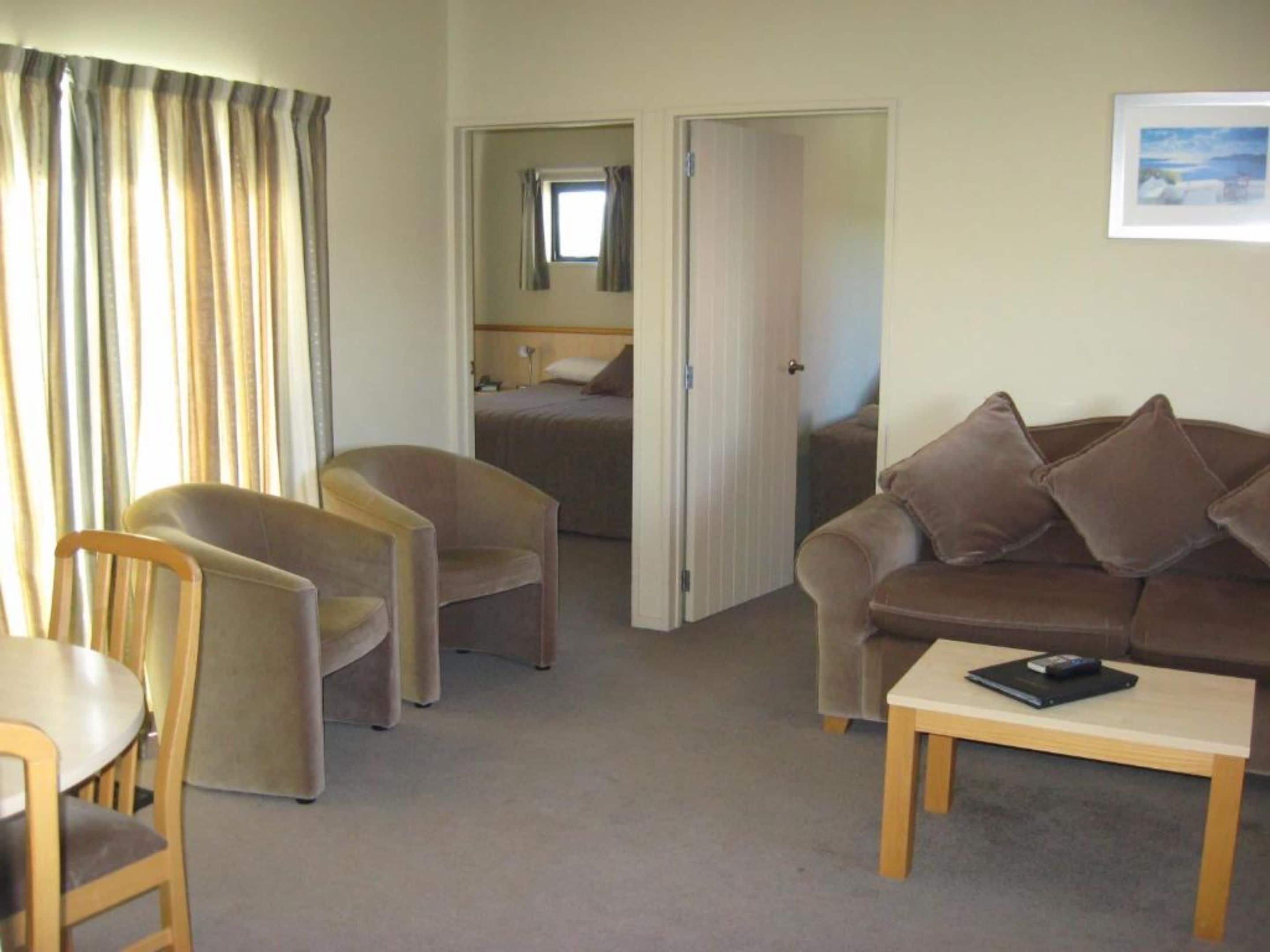 A hotel room with a sofa, two armchairs, a small table, and a bed with a window.