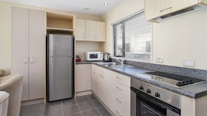 A compact kitchen with a stainless steel refrigerator, a microwave, a gas stove, and a built-in oven. - Kaikoura Gateway Motor Lodge (Kaikoura)