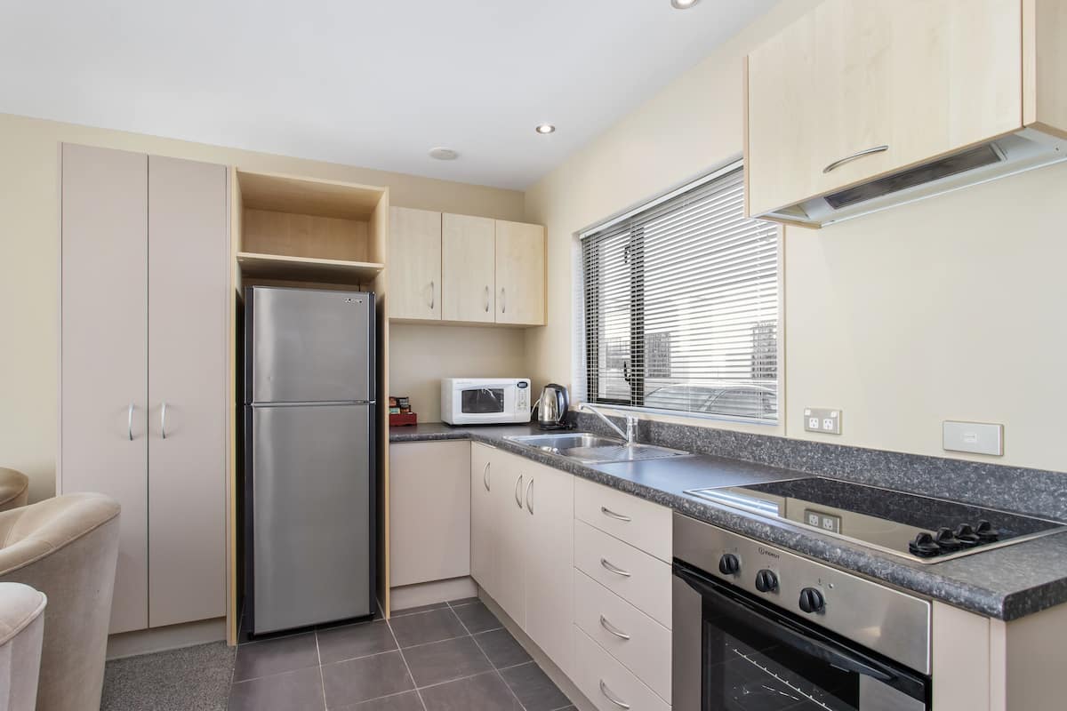 A compact kitchen with a stainless steel refrigerator, a microwave, a gas stove, and a built-in oven.