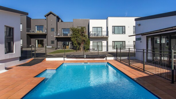A modern pool area with a rectangular pool, surrounded by a black fence, and adjacent buildings with balconies and windows. - Kaikoura Gateway Motor Lodge (Kaikoura)