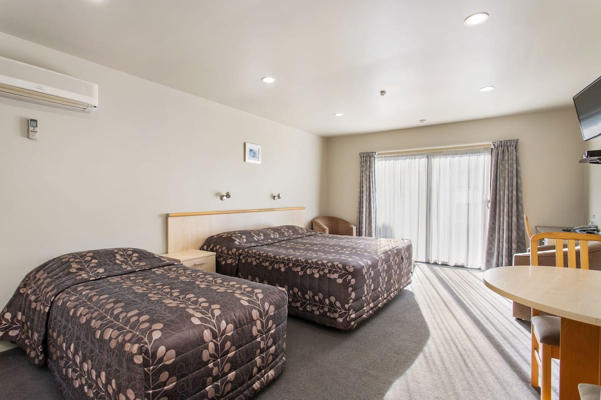 A hotel room with two beds, a desk, a chair, and a TV.