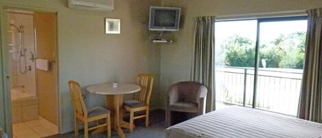 A hotel room with a bed, a TV, a small table with two chairs, and a balcony with curtains.
