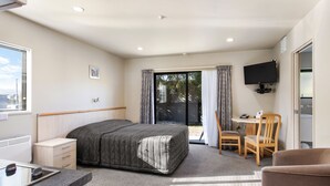 A hotel room with a bed, a desk with a chair, a television, and a sliding glass door leading to an outdoor area. - Kaikoura Gateway Motor Lodge (Kaikoura)