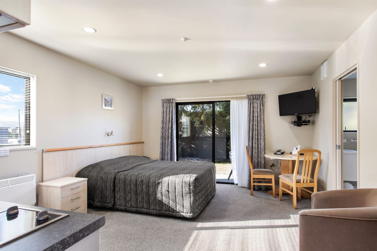 A hotel room with a bed, a desk with a chair, a television, and a sliding glass door leading to an outdoor area.