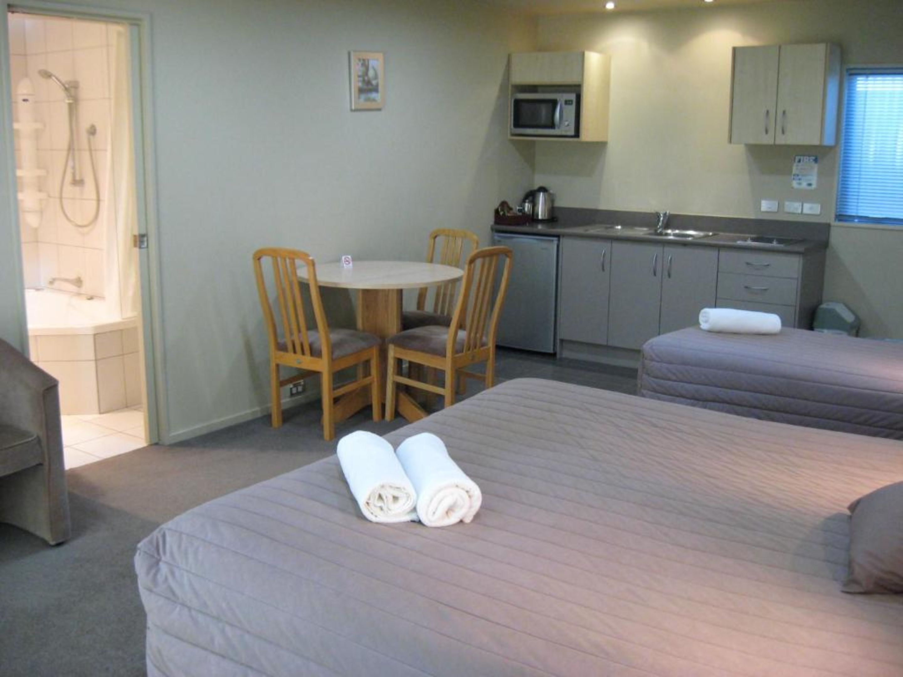 A hotel room with a bed, two chairs, a small table, a microwave, and a sink.