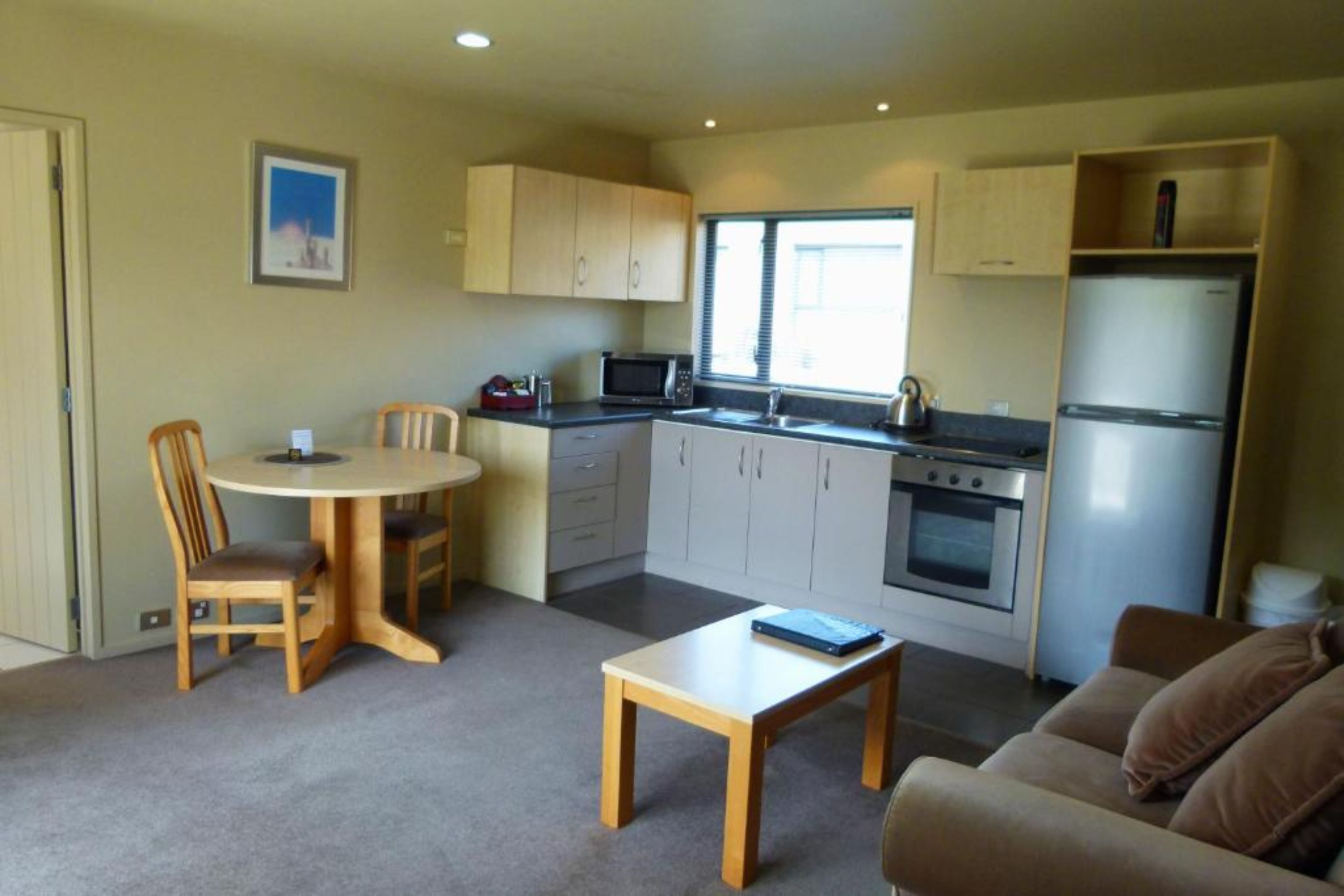 A compact kitchen with a dining table, chairs, a refrigerator, and a microwave.