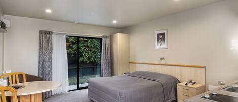 A modern hotel room with a bed, a small desk, a chair, a window with curtains, a sink, and a framed picture on the wall.