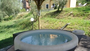 A hot tub with a surrounding deck, a pergola, and a grassy area with trees and a building in the background. - Casali Romei - Apartments (Sarzana)