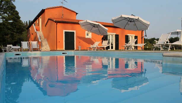 A swimming pool with lounge chairs and umbrellas, a building with orange walls, and a staircase leading to an upper level. - Casali Romei - Apartments (Sarzana)