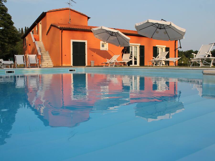 A swimming pool with lounge chairs and umbrellas, a building with orange walls, and a staircase leading to an upper level.